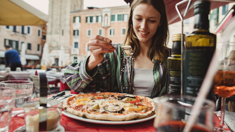 Traveler sprinkling cheese on pizza