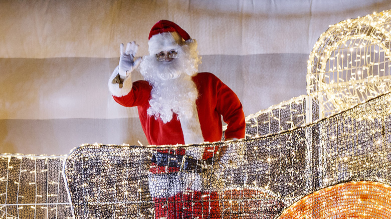 Santa waves next to Christmas lights