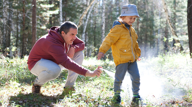 Man spraying son with insect repellent in the forest