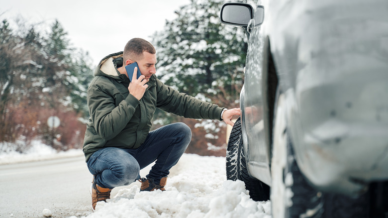 Man checking tire on snowy road