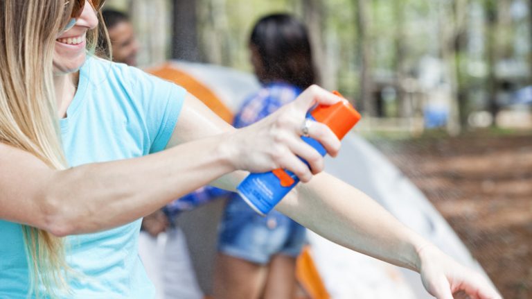 woman spraying bug spray outside